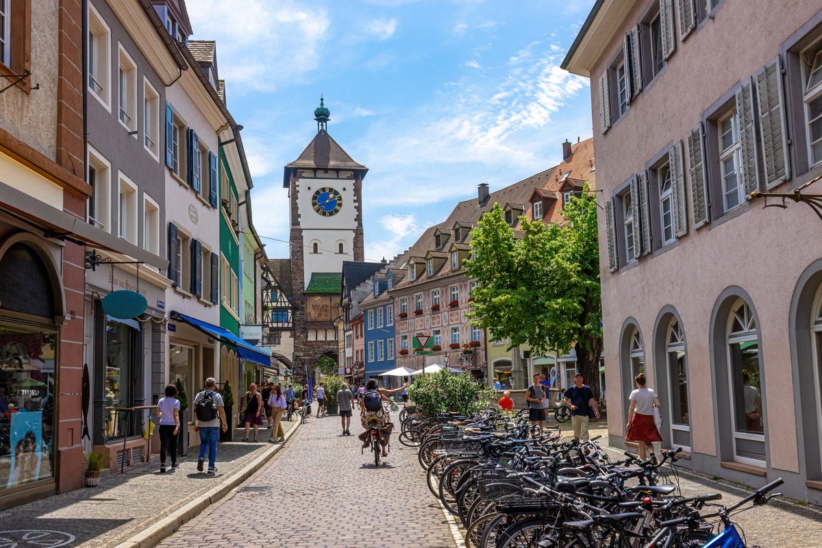 Die belebte Fahrradstadt Freiburg im Breisgau: Blick durch eine historische Gasse auf das mittelalterliche Schwabentor mit seinem charakteristischen Uhrturm